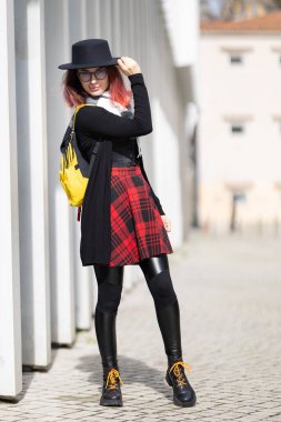 Genç bir kadın güneşli şehir yürüyüşünde alternatif moda kıyafetlerini sergiliyor.