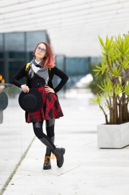 Ekose etekli ve çizmeli şık şehir kıyafetleriyle poz veren genç bir kadın.