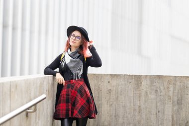 Dışarıda poz veren şık bir kadın, modern bina arka planına sahip beton bir duvara yaslanmış.