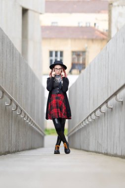 Şık giyinmiş genç bir kadın beton bir yolda dikilip kameraya bakıyor.