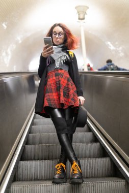 Yürüyen merdivendeki genç kadın, akıllı telefon içeriğine sinirli bir ifadeyle tepki veriyor.