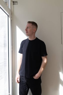 Pencere kenarında duran, başka tarafa bakan, düşünen ve düşünen bir adam.