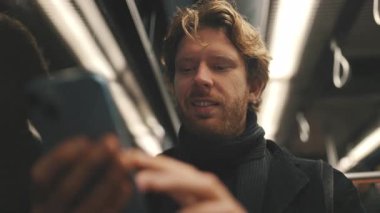 Beyaz adam metroda ya da otobüste seyahat ederken cep telefonuyla kayıyor.