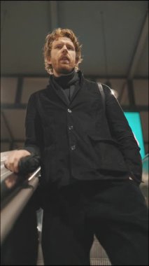 Şık bir adamın modern bir binadaki yürüyen merdivende yükselişinin düşük açılı görüntüsü.