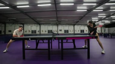 Atletik çift, kapalı bir spor salonunda masa tenisi oynuyorlar.