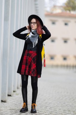 Genç bir kadın dışarıda poz veriyor, şapkasını düzeltirken başka tarafa bakıyor.