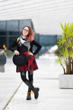 Gözlüklü, kendine güvenen, kendine has tarzı olan modern mimarisi olan, açık havada duran genç bir kadın.