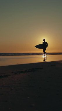 Gün batımında kıyıda koşan bir sörfçünün silueti. Orta çekim