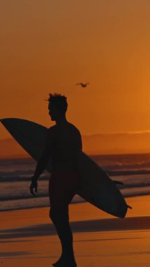 Parlak turuncu gün batımında okyanusa giden bir sörfçünün silueti. Orta çekim