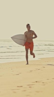 Sörf tahtasıyla sahilde koşan bir sörfçü.