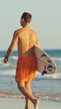 Genç sörfçü elinde sörf tahtasıyla sahilden uzaklaşıyor.