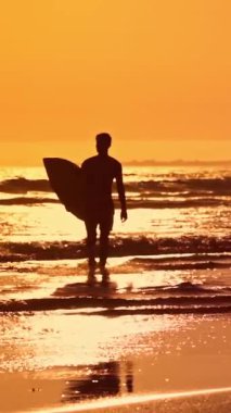 Gün batımında okyanustan çıkan bir sörfçünün silüeti.