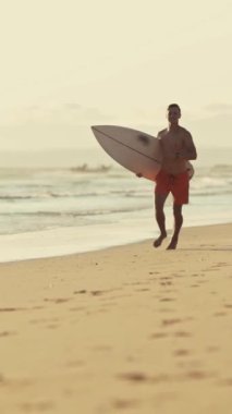 Genç sörfçü sörf tahtasıyla sahilde koşuyor.