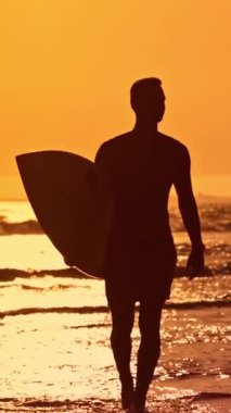 Gün batımında okyanustan çıkan bir sörfçünün silüeti.