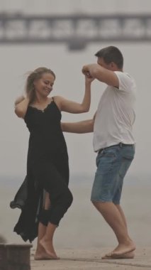 Güzel, romantik, evli bir çift bulutlu havada arka planda köprüyle iskelede dans ediyor. Orta çekim