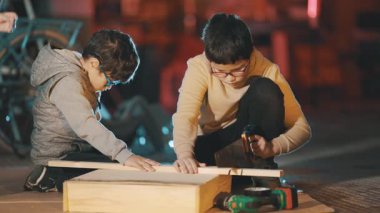 Bir marangozluk projesinde çalışan üç odaklı çocuk, ahşap kesmek ve inşa etmek için el aletleri kullanıyorlar.