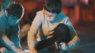 Gözlüklü genç çocuklar birlikte çalışıyorlar ve bir atölyede ahşap bir kalas kesmeye konsantre oluyorlar.