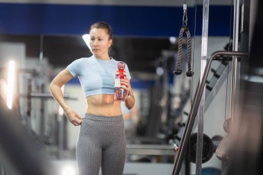 Bir kadın modern bir spor salonundaki şişeden su içiyor.