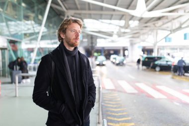 Genç adam havaalanı ya da istasyon girişinde sabırla bekliyor.