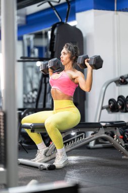 Kadın dambıllarla omuz egzersizi yapıyor, güç ve zindeliğe odaklanıyor.