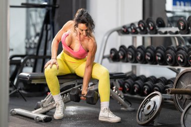 Spor salonundaki halterin üstünde halterle biseps yapan atletik kadın.