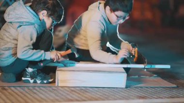 İki meraklı çocuk gece bir ağaç projesinde çalışırken çekiç ve testere kullanıyor.