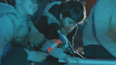 Odaklanmış çocuk bir atölyede ahşap bir tahtaya delik açarak ahşap öğreniyor.