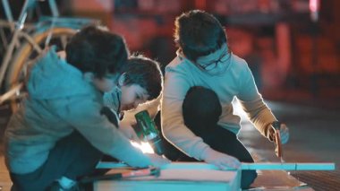 Üç çocuk bir marangozluk projesinde birlikte çalışıyorlar. Geceleri testere, matkap ve çekiç kullanıyorlar.