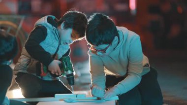 Gece matkap ve el testeresi kullanarak bir marangozluk projesinde çalışan genç çocuklar.