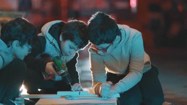 Üç çocuk bir atölyede marangozluk projesinde işbirliği yapıyor.