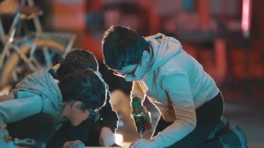 Bir grup genç, kablosuz matkap kullanarak bir marangozluk projesinde birlikte çalışıyorlar.