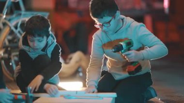 Çocuklar bir-kendin-yap projesinde işbirliği yapıyorlar, marangozluğu öğreniyorlar ve elektrikli aletler kullanıyorlar.