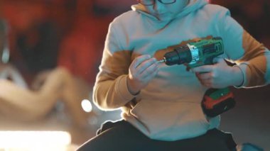 Gözlüklü genç, çocuklar için ahşap işçiliği sınıfında kablosuz matkap kullanmayı öğreniyor.