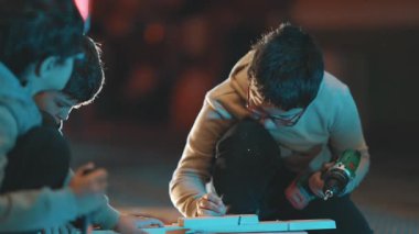 İki meraklı çocuk odundan bir şey yapıyor ve okul projesi için elektrikli matkap kullanıyorlar.