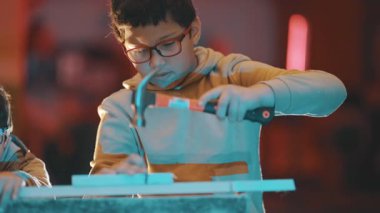 Marangozluk dersi sırasında çekiç ve çivi kullanarak tahta tahtaya odaklanmış çocuk.