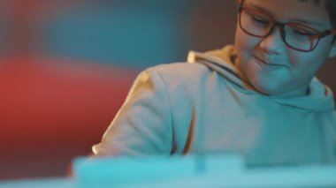 Yetenekli ve gözlüklü bir çocuk neşeli bir şekilde ortamı aydınlatan bir odada sentezleyici klavye çalıyor.