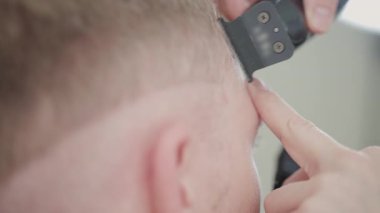 Modern bir kuaförde tıraş makinesi kullanan bir adamın saçını kesen profesyonel bir berber.