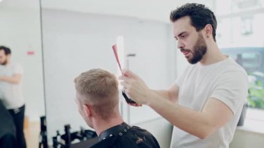 Erkek kuaför modern bir berber dükkanında tarak ve budayıcı ile saç kesimi yapıyor.
