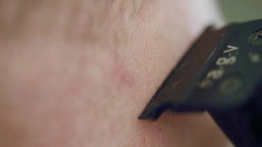 Bir traş bıçağının aşırı yakın çekimi hassas ve tahriş olmuş bir adamın sakalını kesiyor.