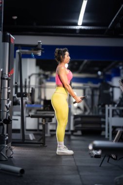 Atletik kadın biseps yapıyor, spor salonunda güç ve forma odaklanıyor.