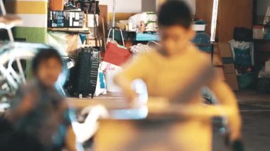 Üç meraklı kardeş, bir ev atölyesinde kablosuz matkap kullanarak birlikte ahşap bir proje inşa ediyorlar.