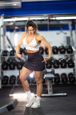 Sporcu kadın gülümsüyor, spor salonunda kendine güvenini ve gücünü ifade ediyor.