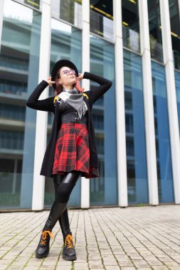 Genç bir kadın, modern şehir ortamında güven içinde poz verirken yukarı bakıyor.