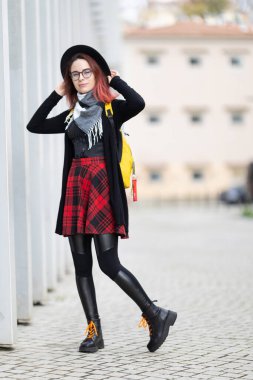 Genç bir kadın dışarıda poz veriyor, alternatif bir etek giyip sırt çantası takıyor.