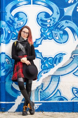 Artistik mavi beyaz desenli bir duvara yaslanan genç bir kadın.