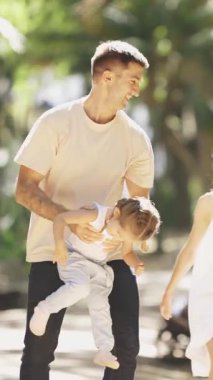 Parkta bir aile yürüyor - ebeveynler kızlarını ellerinde tutuyorlar. Orta çekim