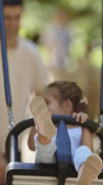 Parkta vakit geçiren bir aile. Ebeveynler kızlarını salıncakta sallıyor. Orta çekim