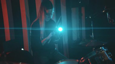 Bir müzik stüdyosunun molası sırasında davul setinde oturan genç bir kadın akıllı telefon kullanıyor.