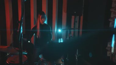 Karanlık bir kayıt stüdyosunda müzik performansı sırasında davul setinde prova yapan enerjik bir kadın.
