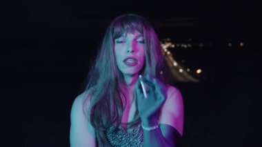 Eflatun renkli transseksüel kadın ve Cyan Light arka planda şehir köprüsü olan bir sigara içiyor.